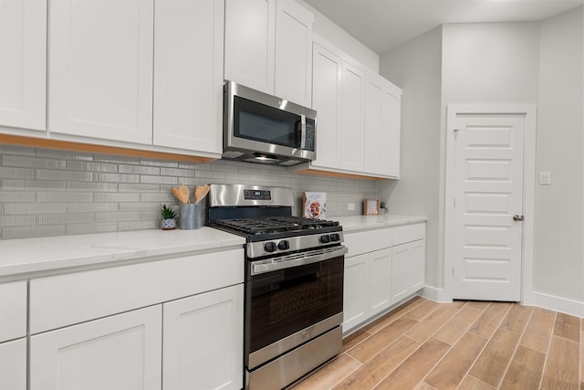 kitchen with white cabinetry, appliances with stainless steel finishes, decorative backsplash, baseboards, and wood tiled floor