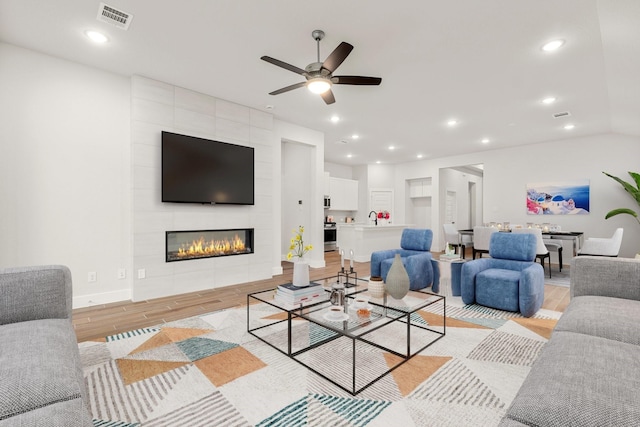 living room featuring a ceiling fan, visible vents, light wood finished floors, recessed lighting, and a tile fireplace