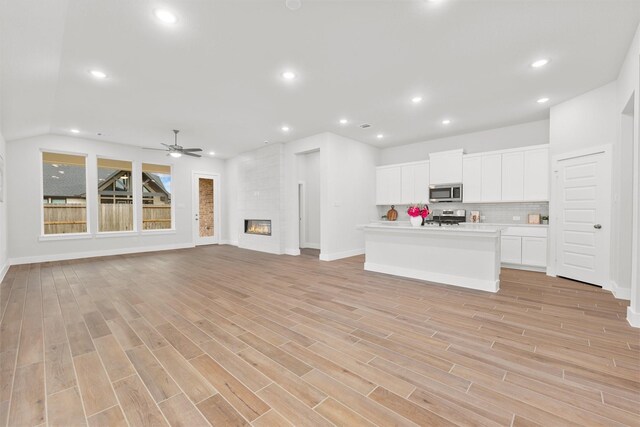 kitchen with a large fireplace, decorative backsplash, light wood-style flooring, appliances with stainless steel finishes, and white cabinets