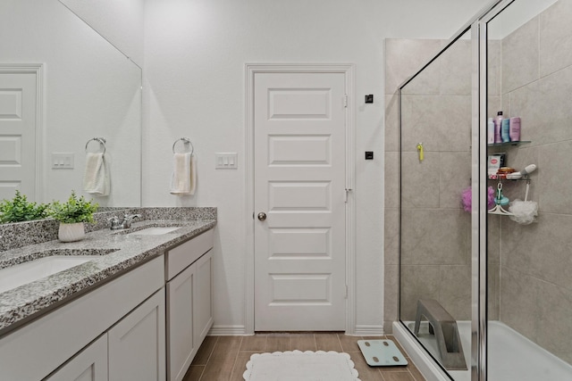 full bath featuring double vanity, a stall shower, wood finish floors, and a sink