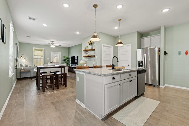 kitchen with visible vents, a sink, open floor plan, appliances with stainless steel finishes, and light stone countertops