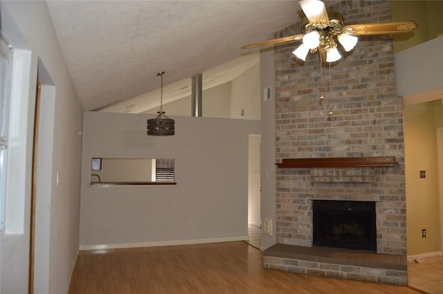 unfurnished living room with wood finished floors, baseboards, lofted ceiling, a textured ceiling, and a brick fireplace