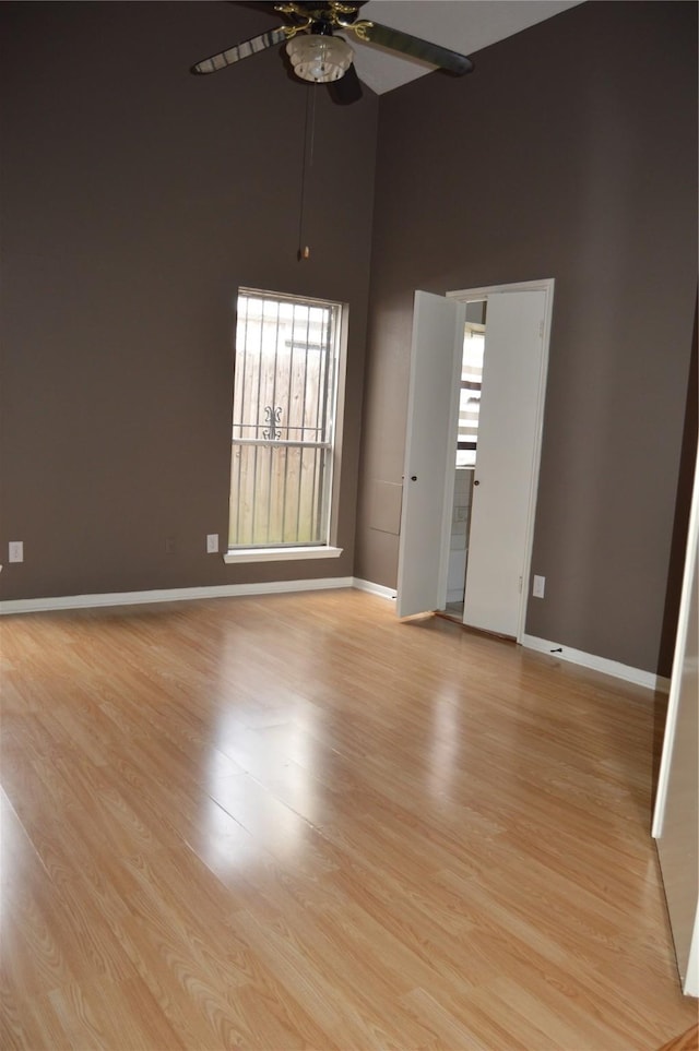 empty room with light wood-style flooring, baseboards, and a towering ceiling