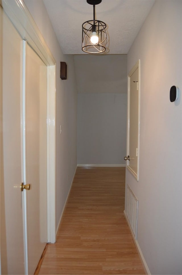 corridor with light wood-style flooring, visible vents, and baseboards