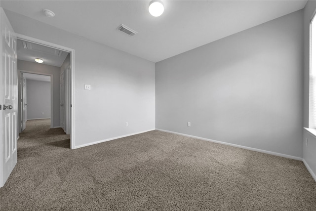 carpeted empty room with visible vents, baseboards, and attic access