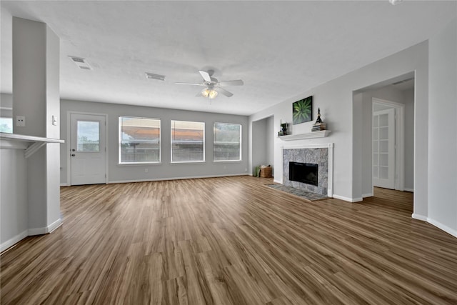 unfurnished living room with wood finished floors, visible vents, a high end fireplace, and ceiling fan