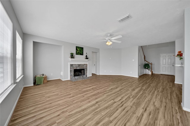 unfurnished living room featuring visible vents, light wood-style flooring, stairs, and a premium fireplace