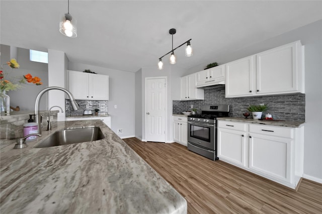 kitchen featuring under cabinet range hood, gas stove, light stone counters, and a sink