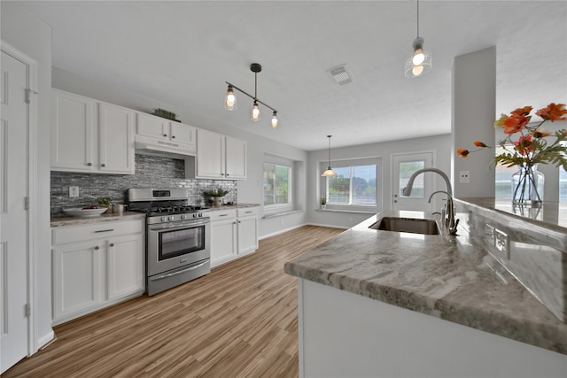 kitchen with stainless steel gas range oven, visible vents, under cabinet range hood, a sink, and white cabinetry