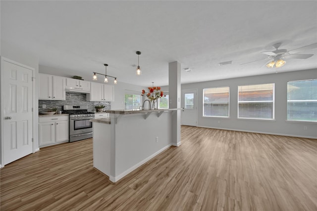 kitchen featuring backsplash, open floor plan, gas range, light wood-style flooring, and white cabinetry