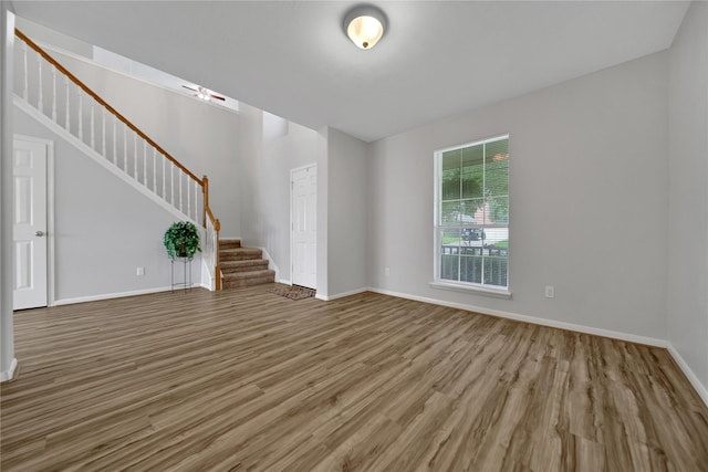 unfurnished living room featuring stairway, wood finished floors, and baseboards