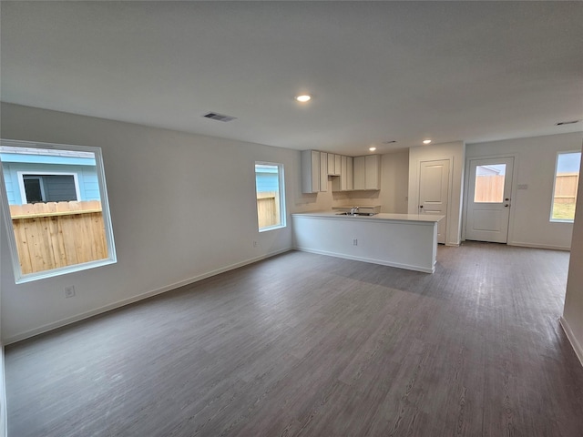 unfurnished living room with visible vents, baseboards, dark wood-type flooring, and plenty of natural light