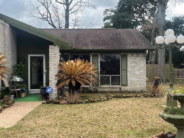 view of property exterior with a yard, fence, brick siding, and roof with shingles