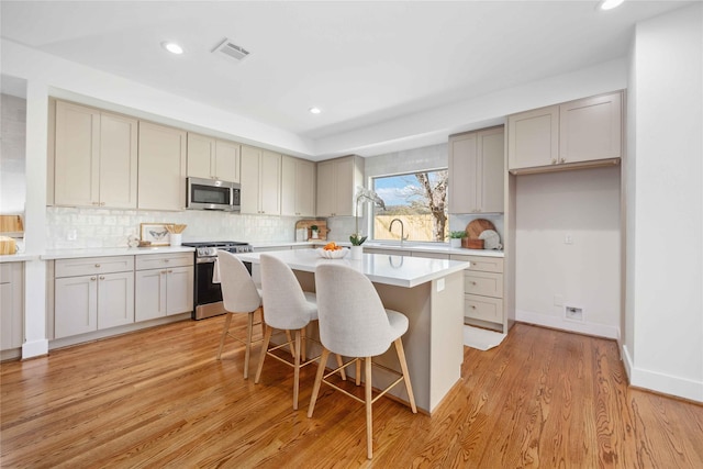 kitchen with visible vents, a kitchen island, light wood-style flooring, stainless steel appliances, and backsplash