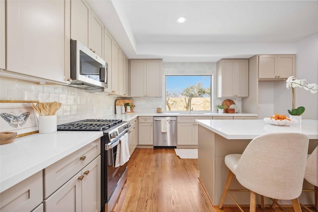 kitchen with light wood-type flooring, a sink, tasteful backsplash, stainless steel appliances, and light countertops