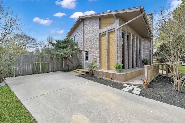 view of property exterior with a wooden deck, a patio area, brick siding, and fence