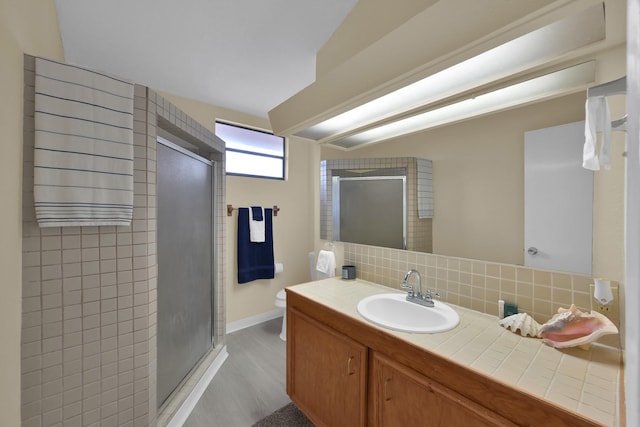 bathroom with vanity, wood finished floors, a stall shower, toilet, and tasteful backsplash