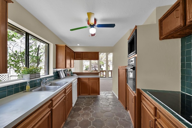 kitchen featuring oven, built in microwave, brown cabinets, white dishwasher, and a sink