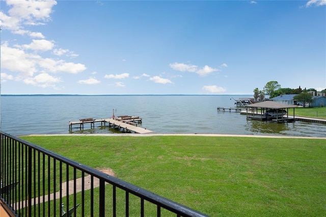 dock area featuring boat lift, a water view, a lawn, and fence