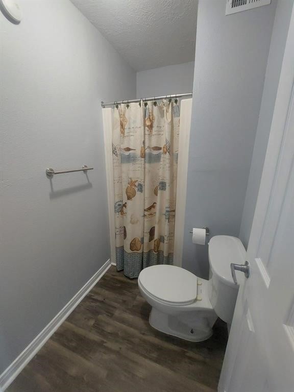 bathroom featuring baseboards, toilet, a shower with curtain, wood finished floors, and a textured ceiling