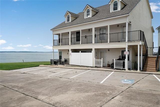 view of front facade featuring stairway, uncovered parking, a water view, and roof with shingles