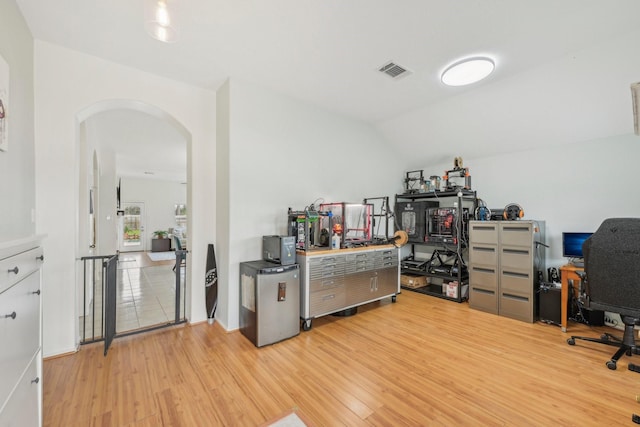 home office with light wood-style floors, arched walkways, visible vents, and lofted ceiling