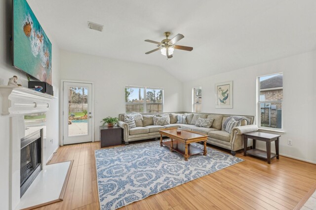 living area featuring lofted ceiling, light wood-style floors, visible vents, and a fireplace with raised hearth