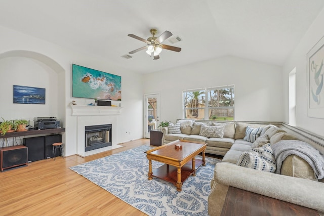 living room with wood finished floors, visible vents, lofted ceiling, a fireplace with flush hearth, and ceiling fan