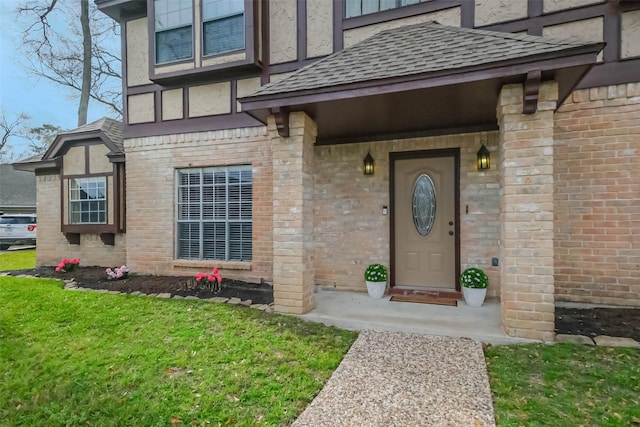 entrance to property featuring brick siding, a lawn, and a shingled roof