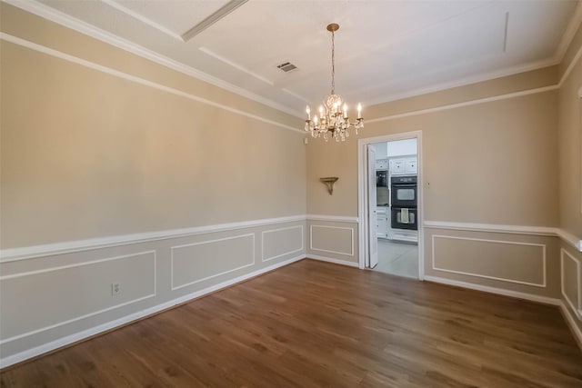 unfurnished dining area with visible vents, crown molding, a chandelier, wainscoting, and wood finished floors