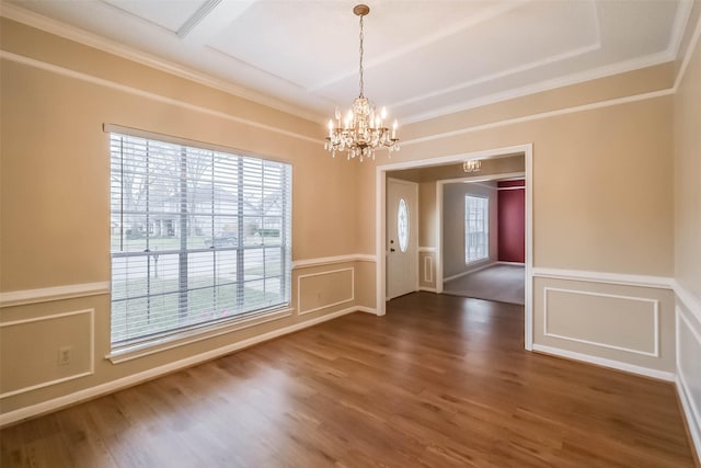 unfurnished dining area with wood finished floors, a wainscoted wall, an inviting chandelier, crown molding, and a decorative wall