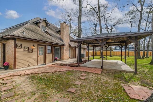 back of house featuring brick siding, fence, a chimney, a yard, and a patio area