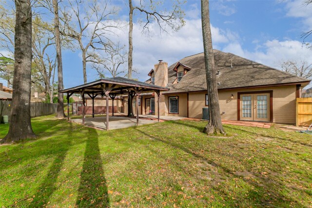 rear view of property featuring a chimney, a gazebo, french doors, a patio area, and a lawn