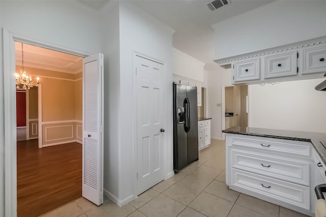 interior space with visible vents, an inviting chandelier, light tile patterned flooring, black fridge with ice dispenser, and white cabinets