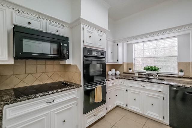 kitchen with dark stone countertops, light tile patterned floors, a sink, black appliances, and white cabinetry