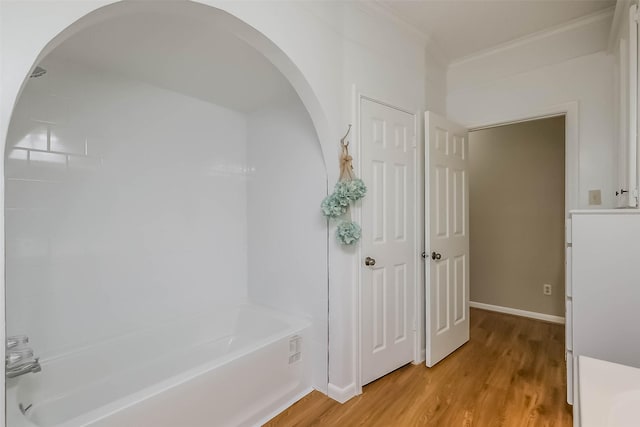 bathroom with ornamental molding, baseboards, bathtub / shower combination, and wood finished floors