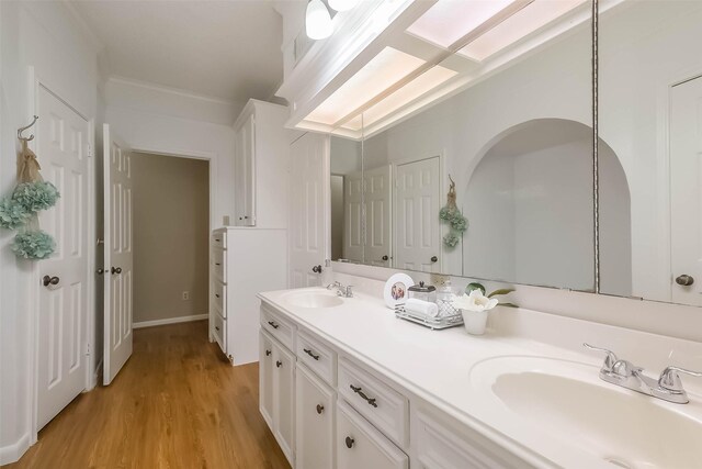 full bath featuring a sink, wood finished floors, double vanity, and ornamental molding