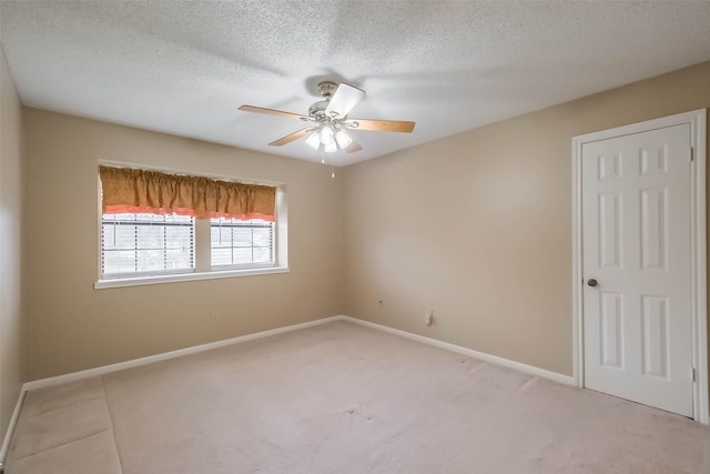 spare room featuring light colored carpet, a textured ceiling, baseboards, and a ceiling fan