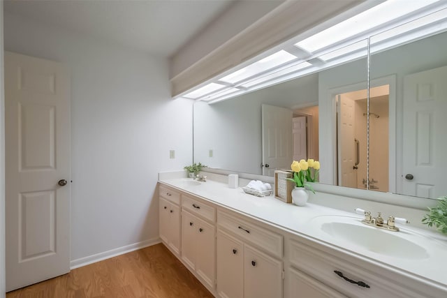 full bathroom featuring a sink, wood finished floors, a skylight, double vanity, and baseboards