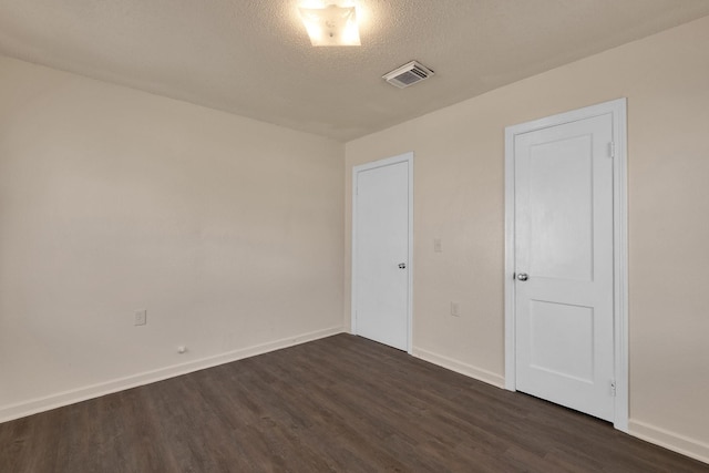 unfurnished room with visible vents, baseboards, a textured ceiling, and dark wood finished floors