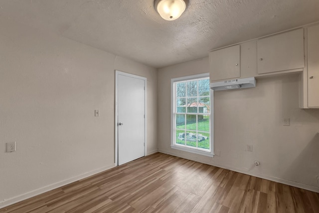 spare room with baseboards, light wood-style floors, and a textured ceiling