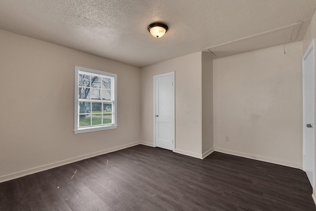 empty room featuring dark wood finished floors, attic access, and baseboards