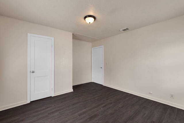 spare room with visible vents, baseboards, a textured ceiling, and dark wood finished floors