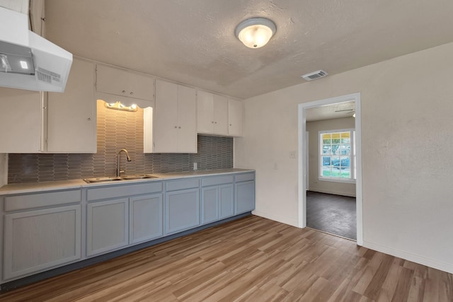 kitchen with visible vents, light wood-style flooring, a sink, light countertops, and decorative backsplash