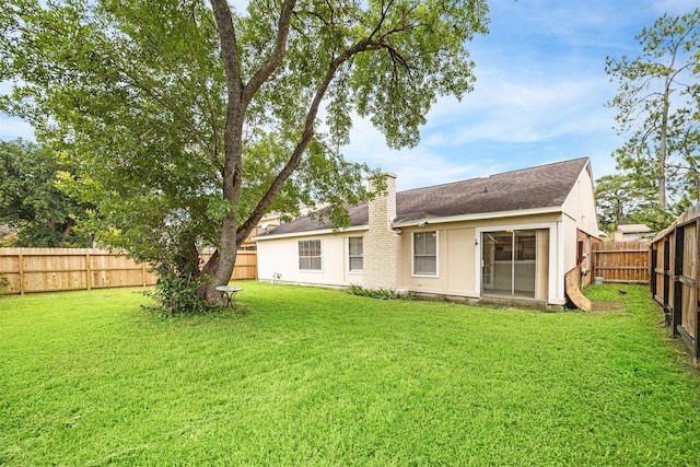 rear view of property featuring a yard, a chimney, and a fenced backyard