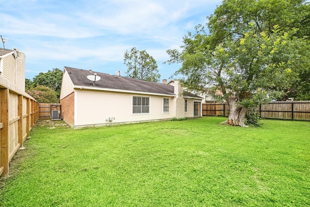 back of property with a fenced backyard, central AC, brick siding, and a yard