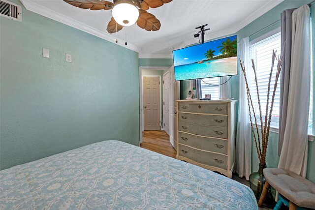 bedroom featuring visible vents, a ceiling fan, wood finished floors, and crown molding