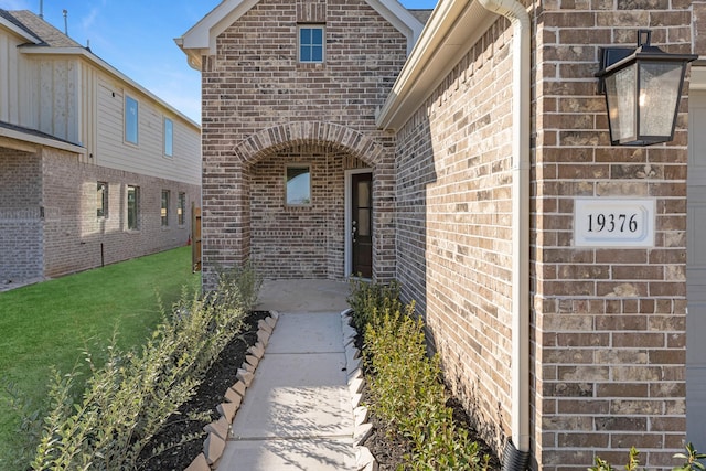 view of exterior entry with a garage, a yard, and brick siding