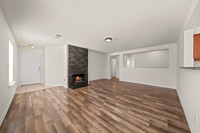 unfurnished living room with visible vents, a textured ceiling, wood finished floors, baseboards, and a tile fireplace