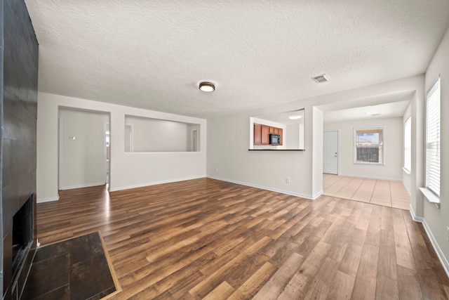 unfurnished living room with visible vents, baseboards, a textured ceiling, and wood finished floors